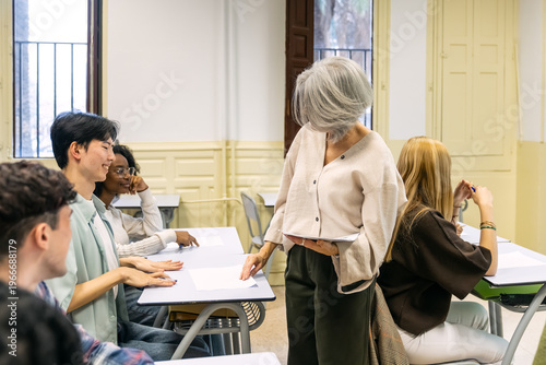 Photography Teacher giving out test papers to a group of smiling, diverse students sitting a