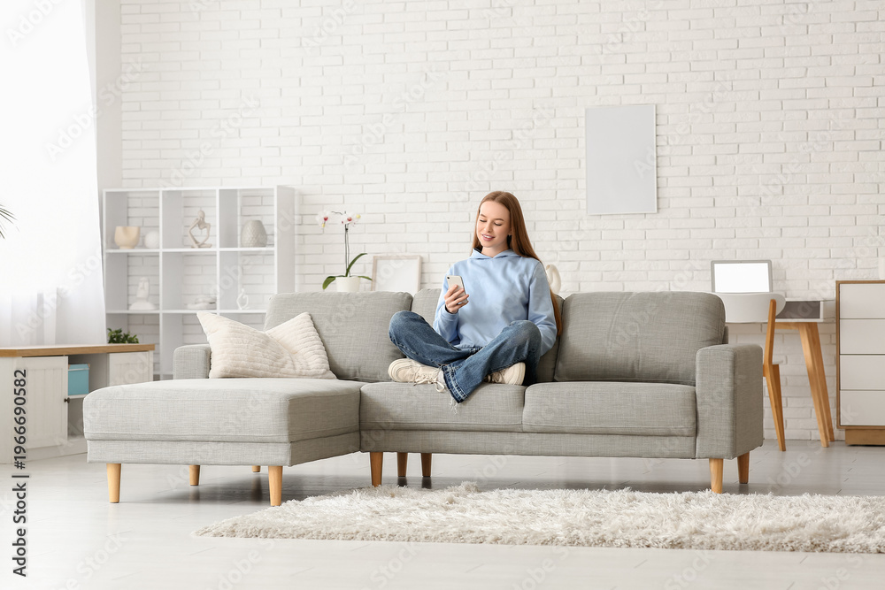 Fototapeta premium Young woman chatting with mobile phone on sofa in stylish living room