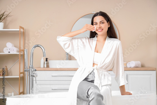 Beautiful young happy woman with cotton pad removing makeup at home
