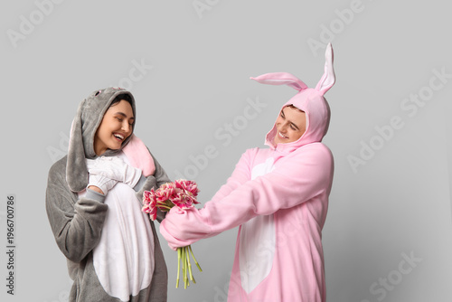 Beautiful young couple in bunny costume with bouquet of tulips on grey backgr...