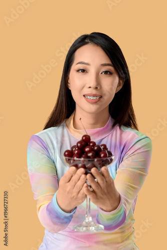 Beautiful Asian woman with sweet cherries on beige background