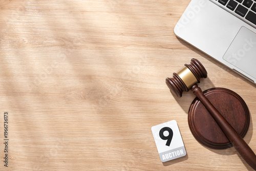 Canvas-taulu Wooden gavel and auction paddle '9' on light wooden desk with laptop, symbolizing online bidding and legal sales