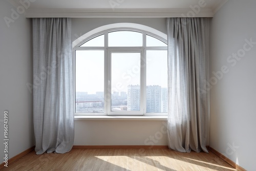 Light gray curtains frame a large arched window overlooking a city view.