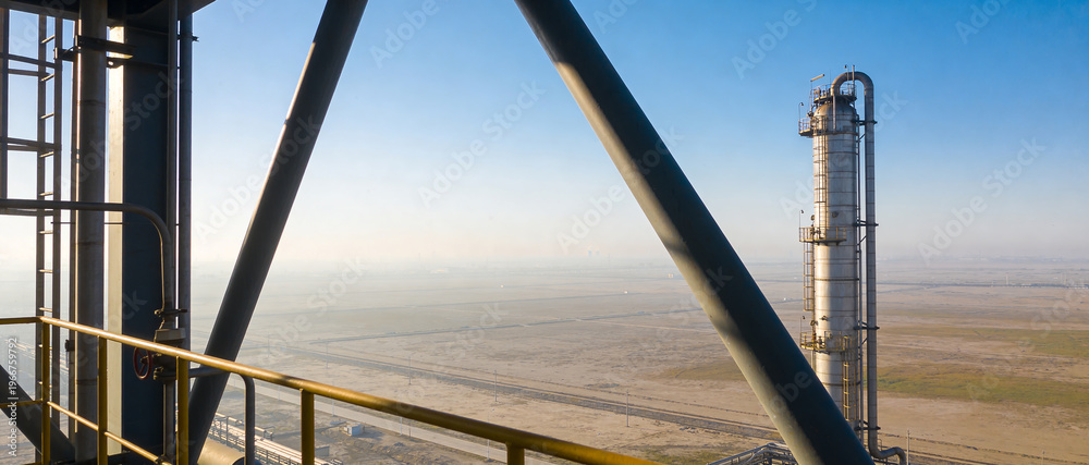 Naklejka premium Panoramic view from an industrial platform looking at a tall distillation tower and vast desert expanses.