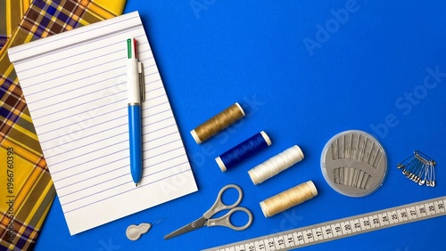 Vászonkép A workbench with sewing tools: scissors, needles, pins, and a tape measure next to a notepad