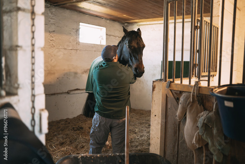 Groom caring for a horse inside a stall, providing companionship and daily care