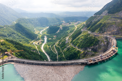 Hydroelectric dam mountain valley reservoir with river and forest slopes, renewable energy, water management, flood control, civil engineering, aerial panorama.