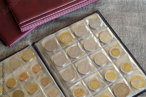 Pages from album full with old coins and burgundy albums for collecting coins. Coin storage method. Numismatic. Close-up. Copy space.