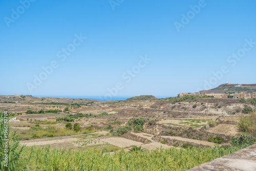 Agricultural fields with sea on the horizon between Gharb and Ghasri with chapel St. Dimitri and Ta' Gurdan lighthouse in the hills, Gozo MALTA
