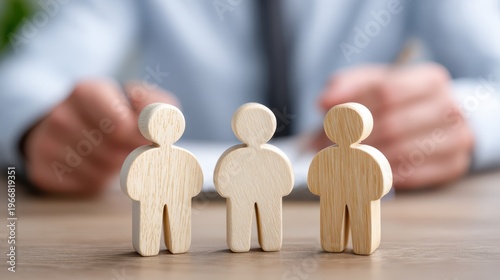 Strategic Alignment: Wooden figurines stand in a row, representing a team or group, with hands of another person or professional background set in the depth.