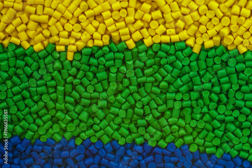 Close-up of a multi-colored layer of blue, yellow, and green plastic pellets for the injection molding process.