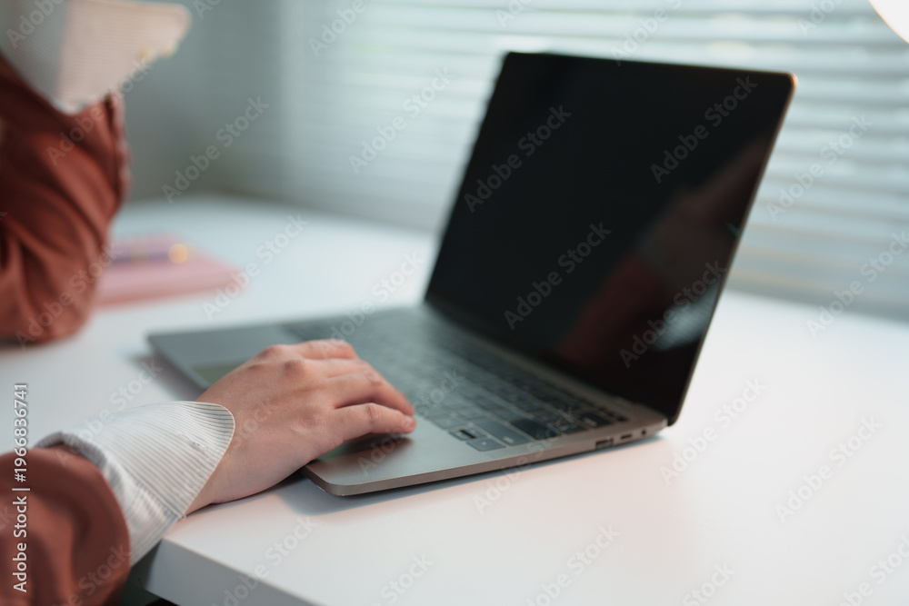 Fototapeta premium Person focusing on work, navigating a laptop's trackpad while sitting at a clean white desk, highlighting remote work flexibility and modern technology usage