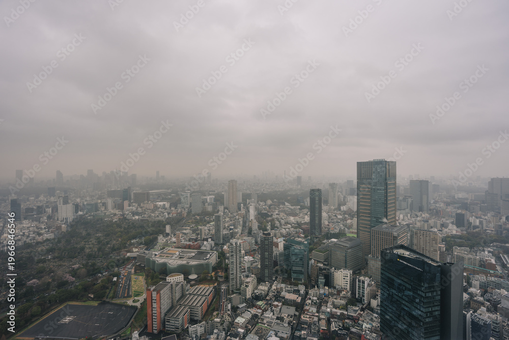 Fototapeta premium Overhead view of a hazy, overcast Tokyo cityscape with towering skyscrapers and a dense urban sprawl.