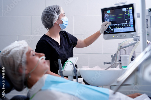 Dental surgery. Woman anesthesiologist is watching life monitor of patient waiting for surgical operation.