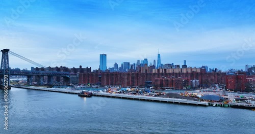 View on the waterfront of the East River with construction in progress. Approaching the Williamsburg Bridge and city skyline at dusk.