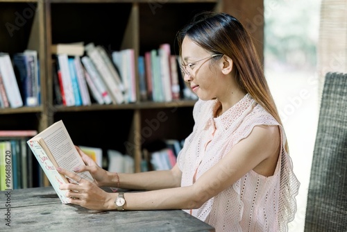 Картината върху платно Woman sitting at a table reading a book in a library setting with bookshelves