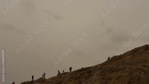 Small Team Of Adventurers Navigates Steep Hills Under Cloudy Skies While Exploring Remote Wilderness