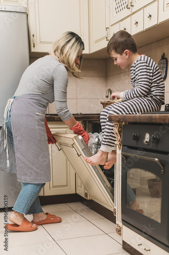 Obraz na plátně A mother and son unload the dishwasher together in the kitchen