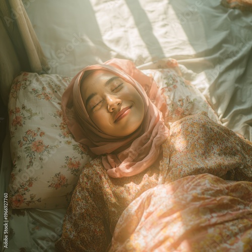 Happy Young Woman Wearing Pink Headscarf Resting in Sunlit Bed Surrounded by Floral Bedding