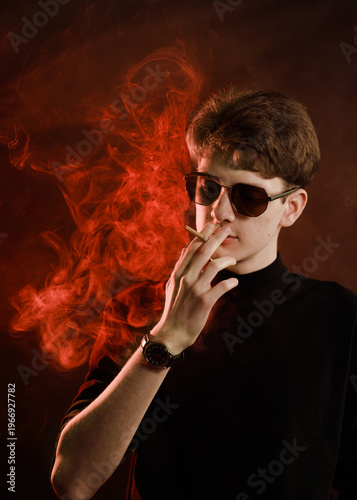 Young man in black turtleneck smoking cigarette in moody red light.