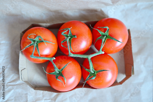 Organic red tomatoes on green branch in eco-friendly paper packaging, top view of healthy farm vegetables for grocery retail.