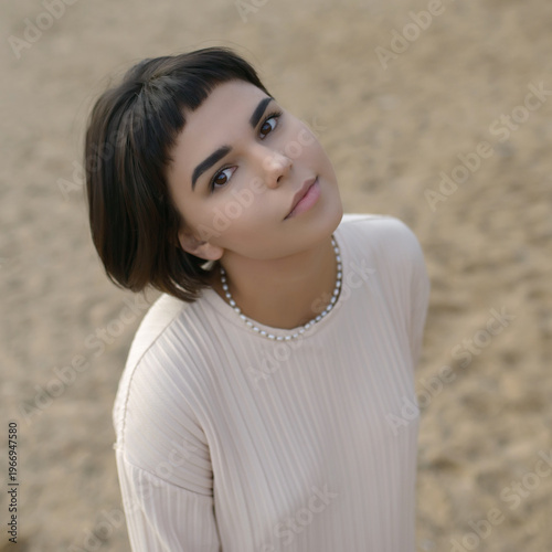 Portrait of thoughtful young woman with short hair on sandy beach.