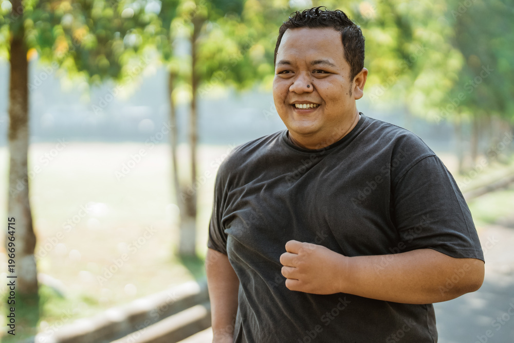 Fototapeta premium portrait of a fat man with a toothy smile jogging in the morning while exercising in the park