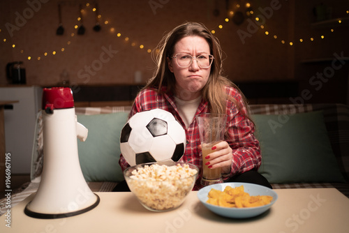 Принти на полотні resentful female football fan holding ball watching soccer game on tv at home sitting on sofa with beer and snacks puffing cheeks