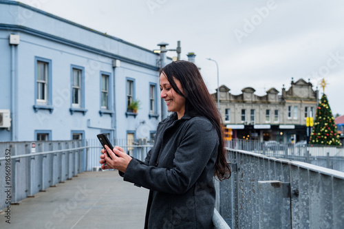 Woman standing on a walkway looking at her mobile phone near a blue building in New Zealand