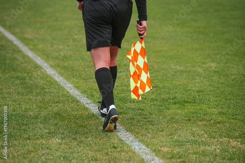 Referee walks grass field holding yellow flag
