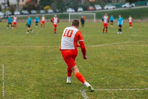 Soccer player wearing a red and white uniform on a grassy field in a rural football game, illustrative image.
