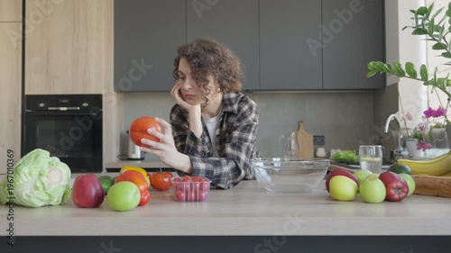Thoughtful Female Holding Tomato In Hand In Bright Modern Home Kitchen