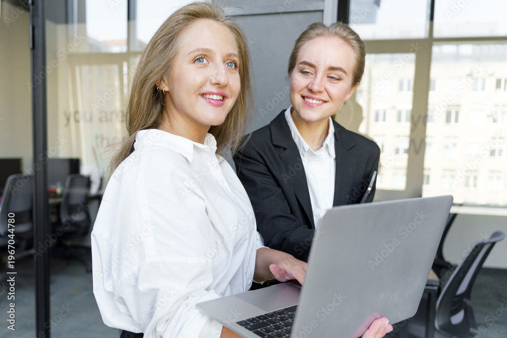 Obraz premium Professional women collaborating on a laptop in a bright modern office setting during daytime hours