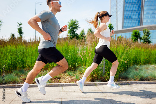 Fotografia Active man and woman jogging side-by-side along a park path on a bright, clear d