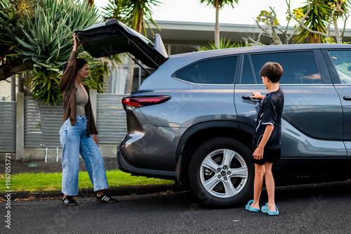 Young boy opening the rear passenger door of the car while mum closes the boot