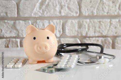 Piggy bank with stethoscope and pills on white table. Health care financial checkup or saving for medical insurance costs concept