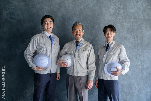 グレー背景で並んで笑顔の作業服を着た日本人男性