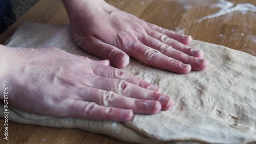 Close-up of rolling dough with a wooden rolling pin on a floured surface. Baking process, homemade pastry preparation, artisan kitchen concept.