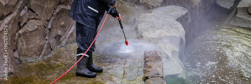 Worker cleaning stone wall with pressure washer removing dirt and algae outdoor