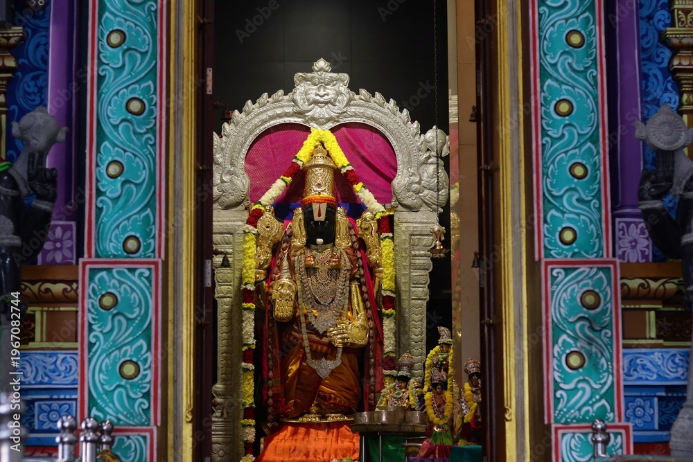 Fototapeta premium Intricately decorated and brightly lit Hindu deity shrine adorned with vibrant colors and flower garlands inside Batu Caves, Malaysia.