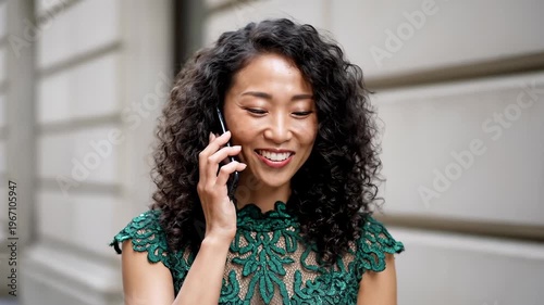 Smiling Asian Woman With Curly Hair Talking on Cell Phone Outdoors, Close Up