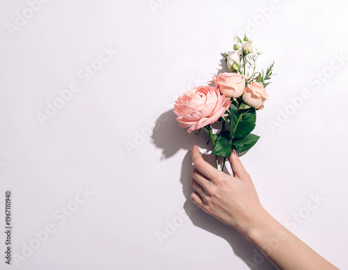 Minimalist Flat Lay Composition of a Female Hand Holding a Small Pink Rose Bouquet against a Plain White Background, with soft, dramatic shadows for a contemporary, stylish look