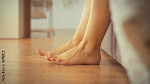 Young girl gently swings her bare feet off bed, stretching them after refreshing morning nap at home. She slowly places her feet floor, marking serene start to her day with natural awakening process