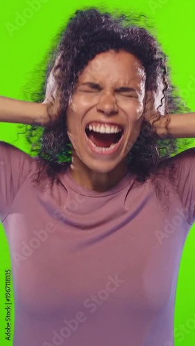 Frustrated young African American woman with curly hair holding ears and screaming in casual clothing on green background. Emotion, stress, anxiety and mental health concept.