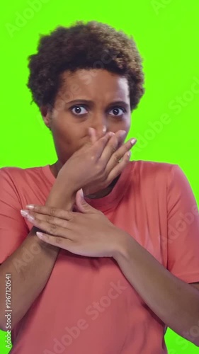 Young African American woman reacts to bad smell holding nose with disgust and surprise on green background. Emotion, reaction and unpleasant odor concept in casual clothing.