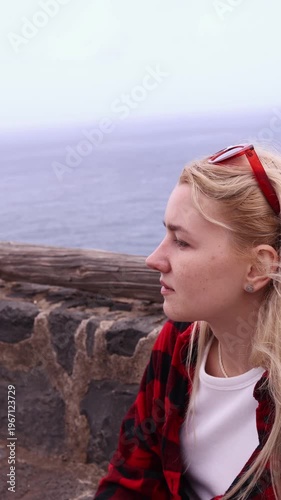 Close-up side profile of thoughtful young blonde woman gazing at Atlantic ocean from volcanic rocks in Tenerife, Canary Islands. Perfect for travel, lifestyle and emotion projects