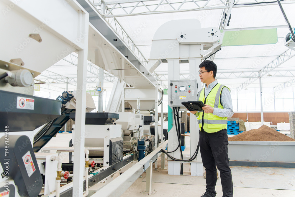 Ταπετσαρία Factory worker in safety vest holding tablet while inspecting equipment on produ