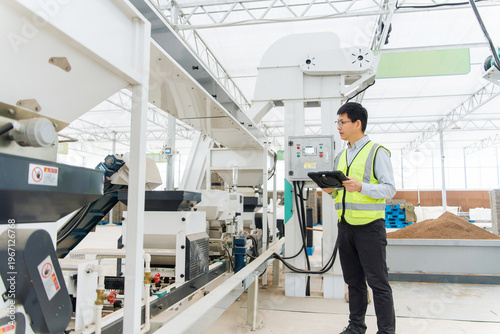 Φωτογραφία Factory worker in safety vest holding tablet while inspecting equipment on produ