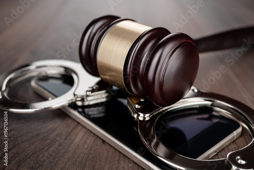 Wooden gavel and handcuffs on smartphone placed on round base. Concepts of court case in technology space and regulation.