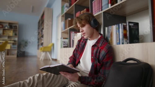 Focused student reading book and listening to music in library
